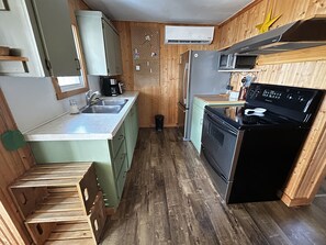 Una cocina compacta con paredes de madera, un lavamanos, una estufa y un refrigerador.