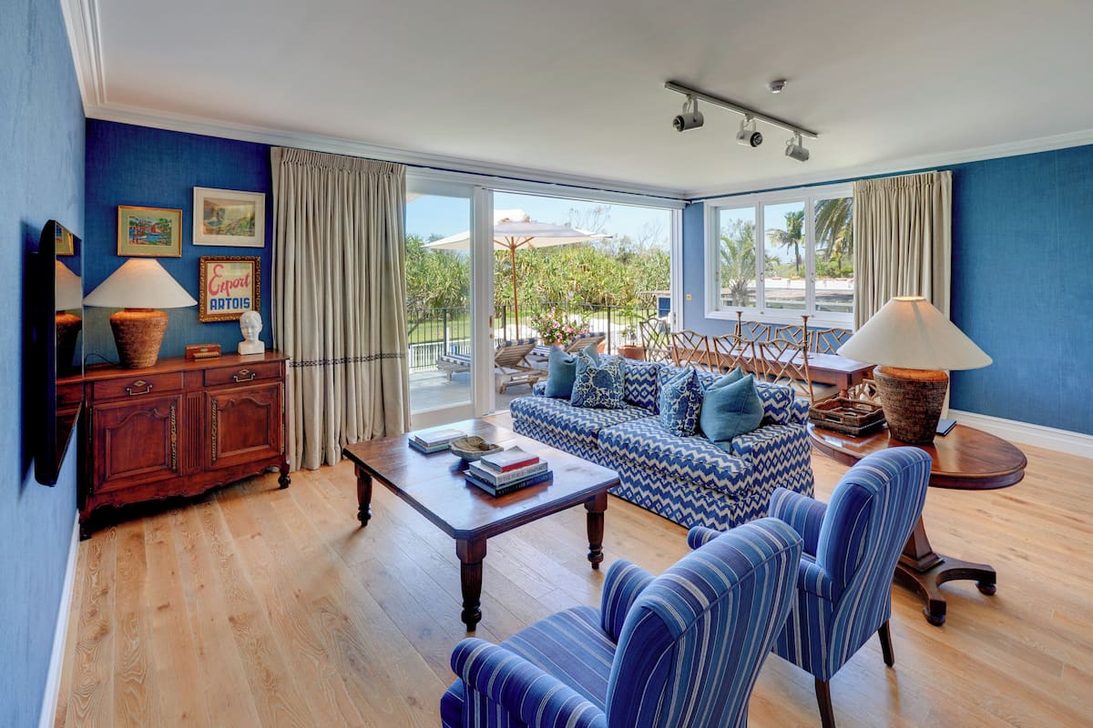 A spacious living room with a blue sofa, striped chairs, a wooden coffee table, and a cabinet with lamps.