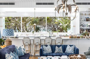 Una sala de estar moderna con un sofá azul, sillas de mimbre y un ventanal con vistas a árboles.