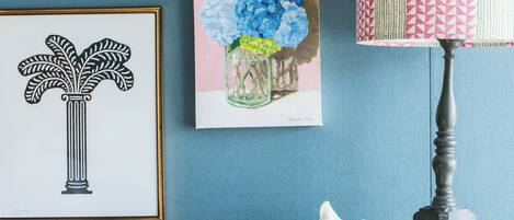 A wall with framed artwork, a lamp, and a small table with books and a basket.