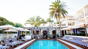 A pool area with lounge chairs and umbrellas, surrounded by palm trees and a building with balconies. - Halcyon House (Cabarita Beach)