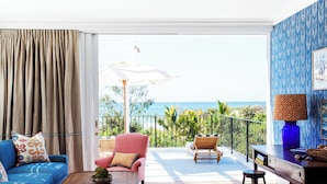 A room with a view of the ocean, a blue sofa, a pink armchair, and a wooden table with a lamp. - Halcyon House (Cabarita Beach)