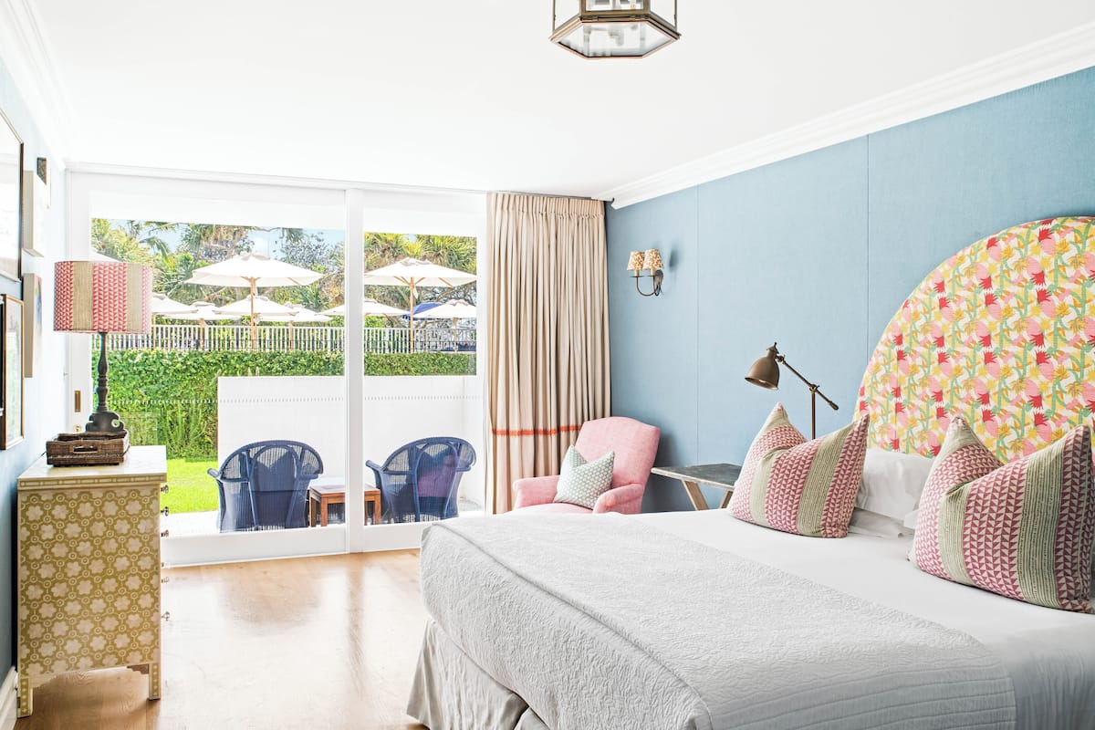 A bedroom with a large bed, a chair, a small table, and a view of an outdoor area with umbrellas.