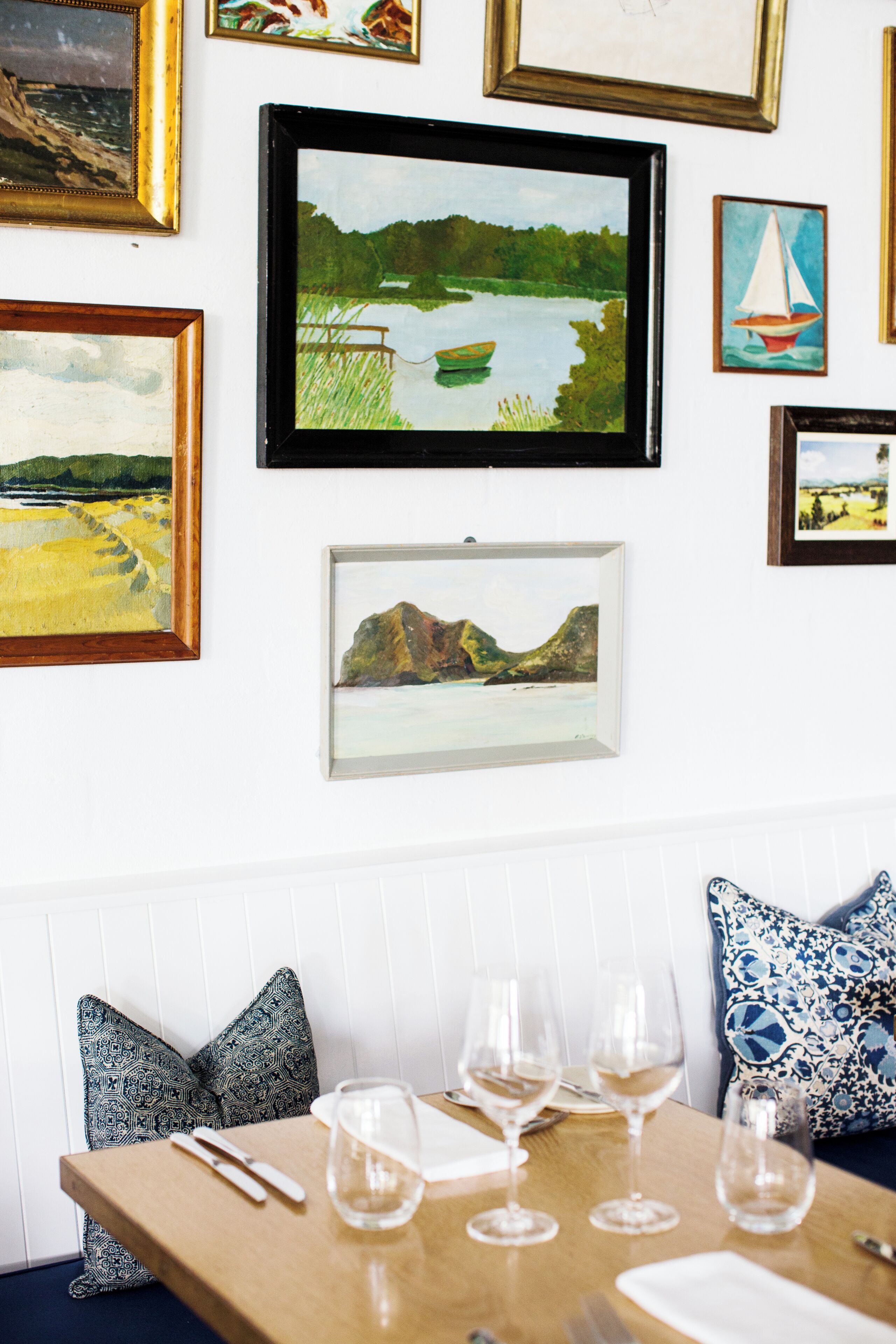 A dining area with a table set for four, surrounded by framed landscape paintings on the wall.
