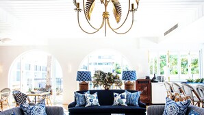 A living room with a dark blue sofa, patterned cushions, a coffee table with books, and a chandelier. - Halcyon House (Cabarita Beach)