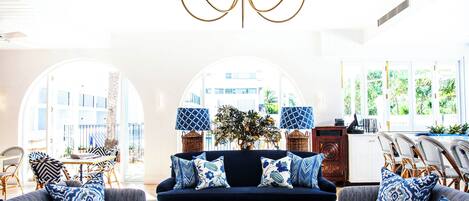 Un salon avec un canapé bleu foncé, des coussins à motifs, une table basse avec des livres et un lustre.