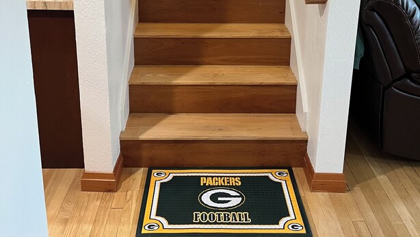 A wooden staircase with a doormat featuring the Packers Football logo.