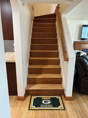 A wooden staircase with a doormat featuring the Packers Football logo.