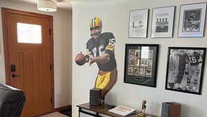 A room with a wooden door, a black leather chair, a desk with a computer, and a wall with framed photos.