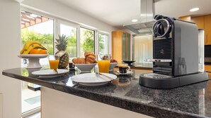 A modern kitchen with a coffee maker, breakfast items, and a view of the outdoors. - Villa da Oliveira with Pool - Golf Aroeira (Herdade da Aroeira)