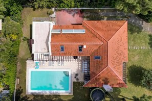 Une maison avec une piscine, une cour clôturée et un toit recouvert de tuiles rouges.