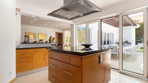 A modern kitchen with wooden cabinets, a black countertop, and a built-in stove. - Villa da Oliveira with Pool - Golf Aroeira (Herdade da Aroeira)