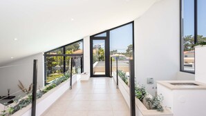 Un intérieur moderne avec un long couloir menant à un espace ouvert, doté de grandes fenêtres, d’un sol carrelé et d’un décor minimaliste.