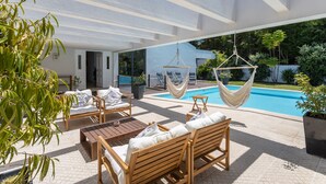 Une terrasse extérieure moderne, dotée de meubles en bois, d’un hamac suspendu et d’une piscine.