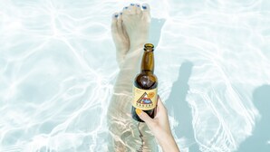 A person holding a bottle of beer with a label, standing in clear water.