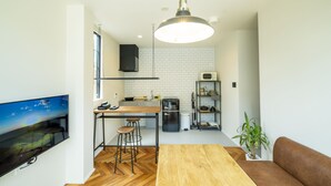 A modern kitchen with a wooden table, bar stools, a TV, and a hanging light fixture. - raw_ (Hakuba)
