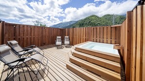 A wooden deck with a hot tub and lounge chairs, surrounded by a wooden fence and mountains in the background.
