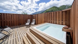 A wooden deck with a hot tub, lounge chairs, and a view of mountains.