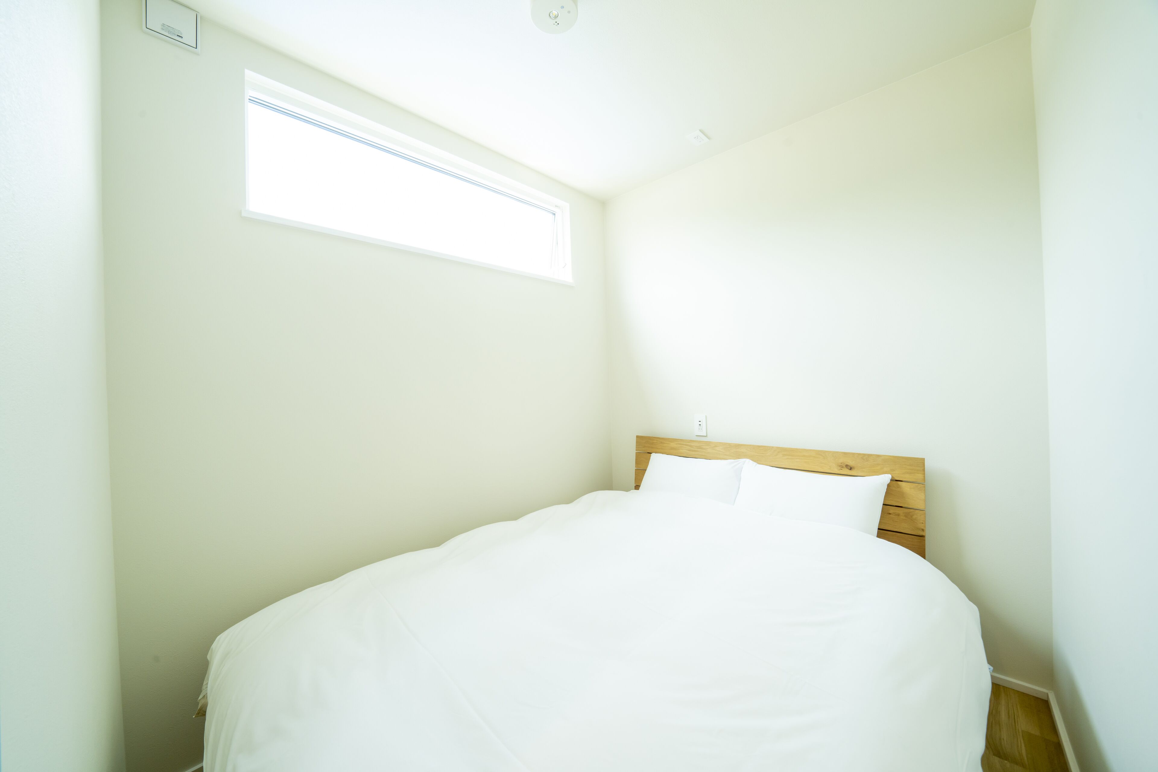 A small, neatly made bed in a corner room with a sloped ceiling and a window.