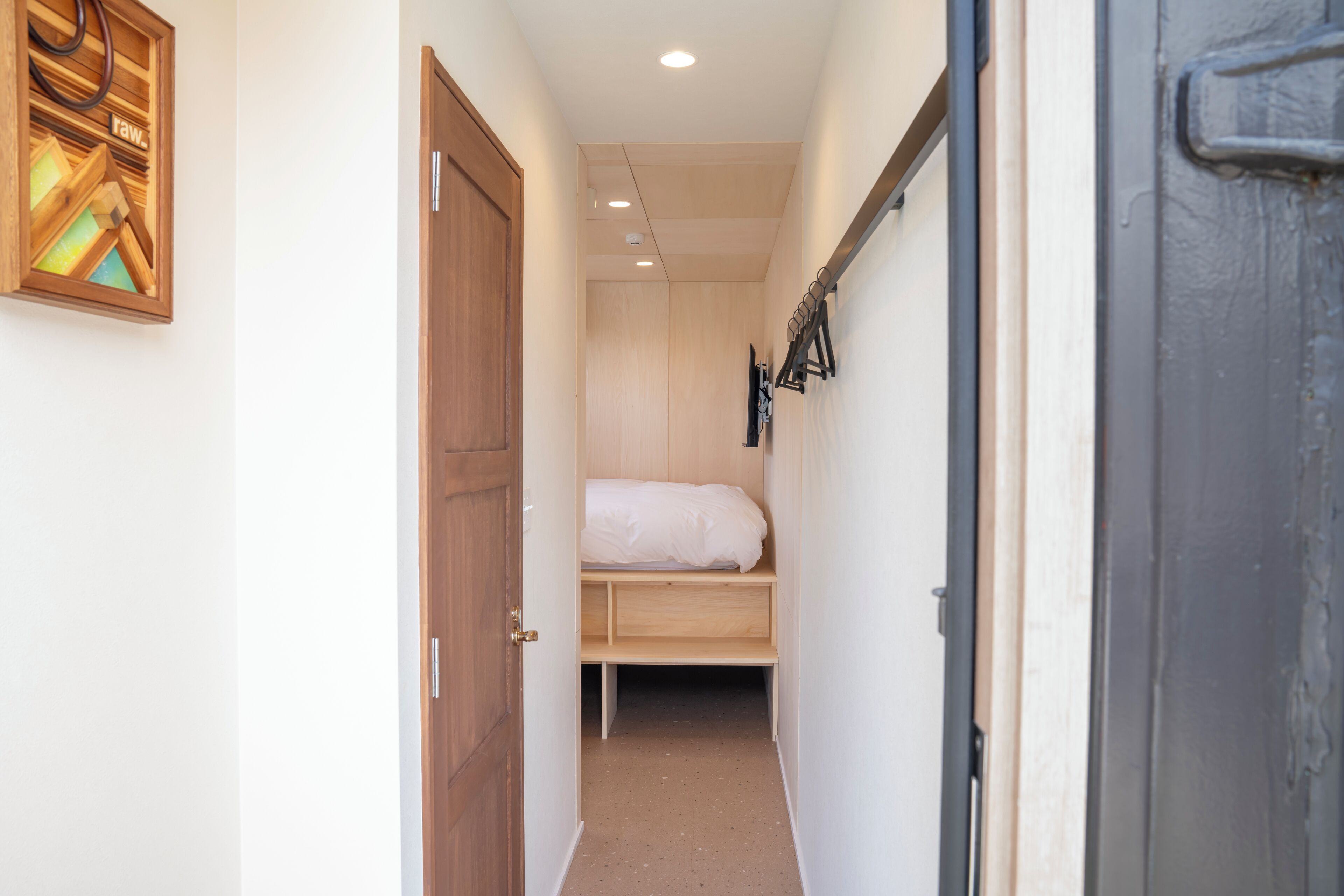 Un pasillo estrecho que lleva a un dormitorio con una puerta de madera, una cama y un perchero en la pared.