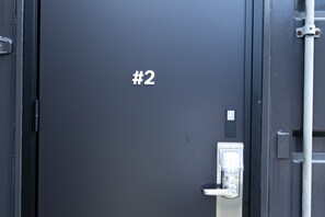 Uma porta escura com fechadura por teclado numérico e placa com o número do quarto.