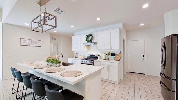 A modern kitchen with white cabinets, a central island with bar stools, a stainless steel refrigerator, and a pendant light. - The Lancaster Gem!

 (Lancaster)