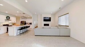 A modern kitchen with a central island, a dining area with chairs, a large white sofa, and a flat-screen TV mounted on the wall. - The Lancaster Gem!

 (Lancaster)