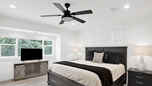 A modern bedroom with a bed, bedside tables, a TV, and a ceiling fan. - Love Shack in Foley/ Hot Tub / Modern Cozy (Foley)