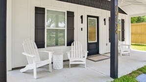A covered porch with two Adirondack chairs and a small trash can. - Love Shack in Foley/ Hot Tub / Modern Cozy (Foley)