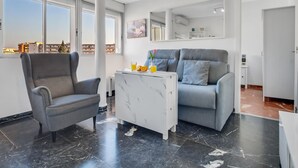 En moderne stue med en grå lænestol, en grå sofa og et sofabord i hvid marmor. Et stort vindue giver udsigt over bybilledet.