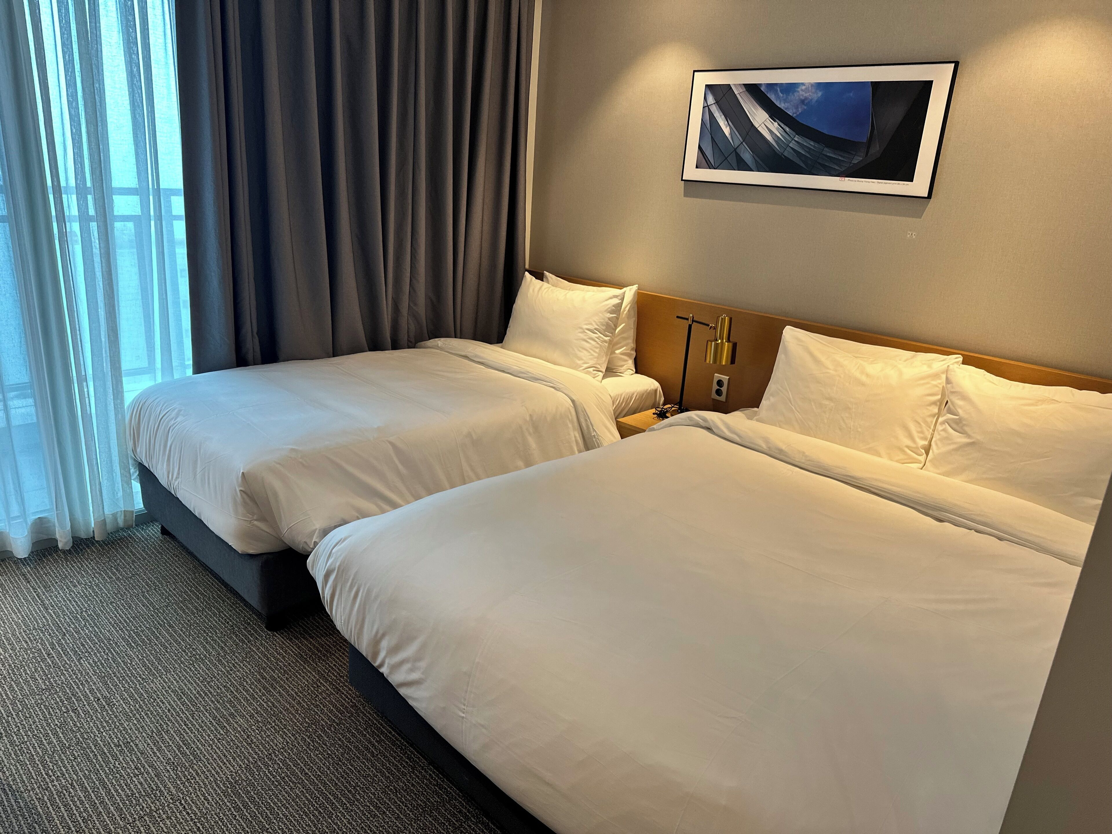 A hotel room with two beds, a nightstand, a lamp, and a framed picture on the wall.