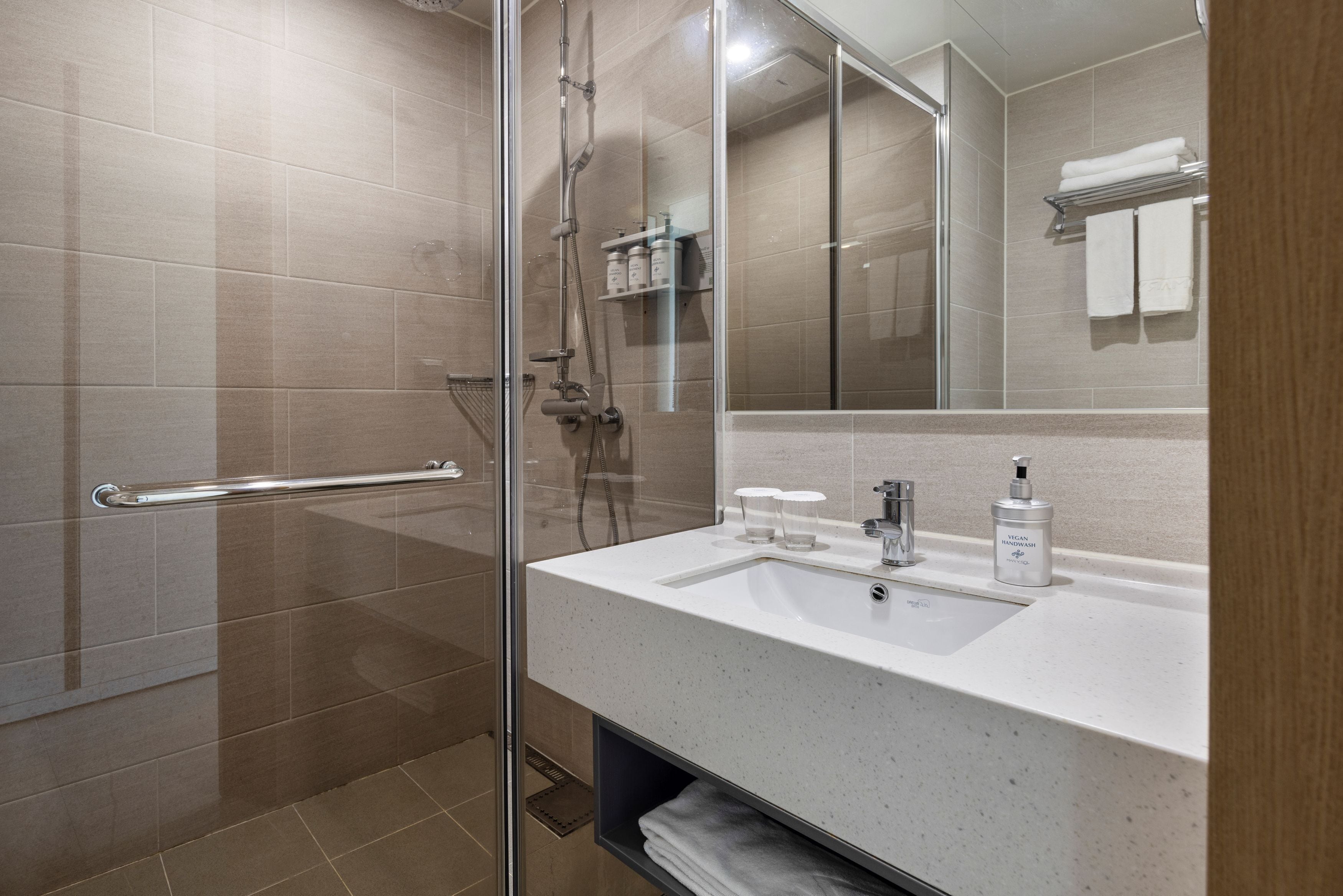 A modern bathroom with a glass shower enclosure, a white sink with a mirror, and a shelf with toiletries.