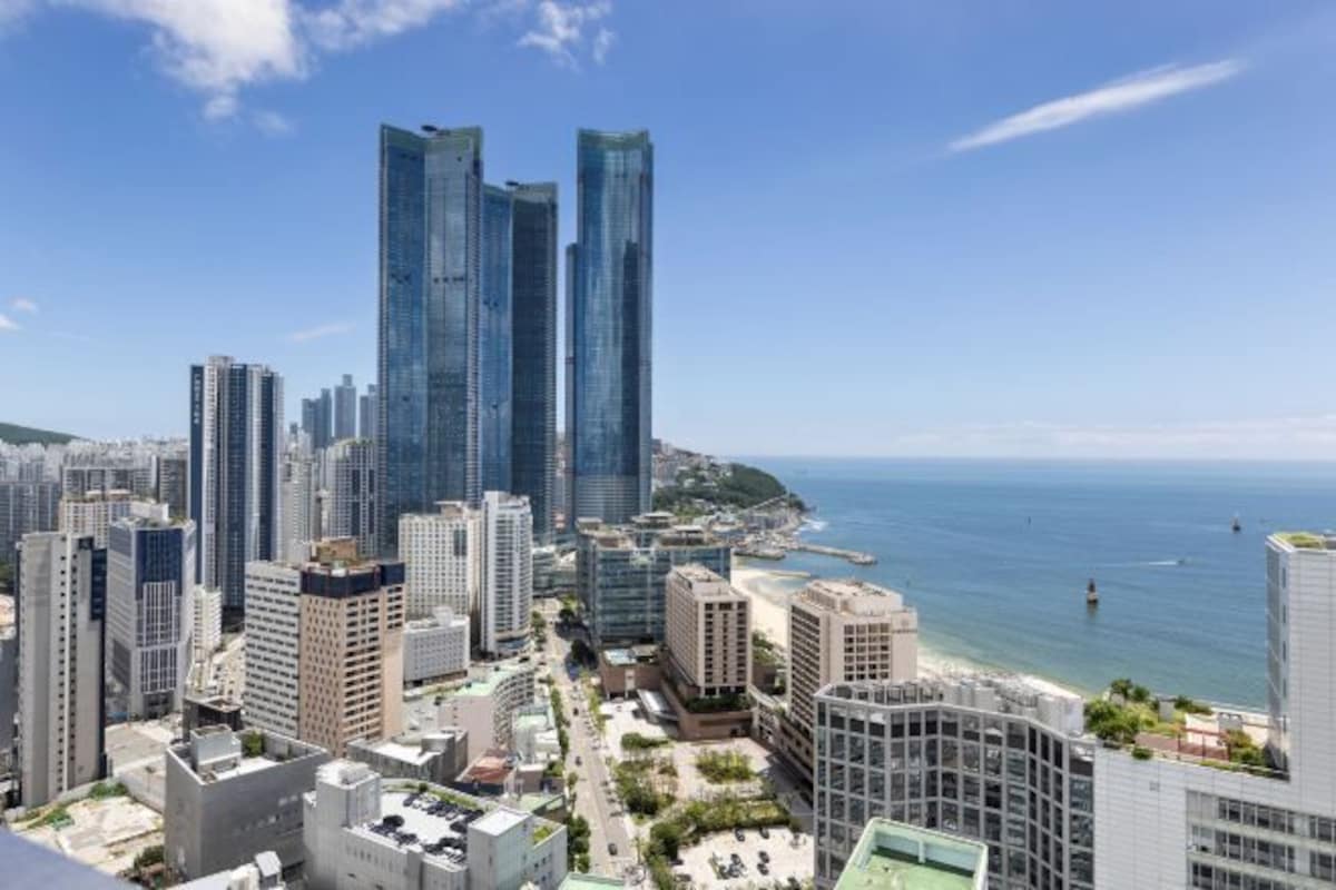 A coastal cityscape with modern high-rise buildings, a beach, and a clear sky.