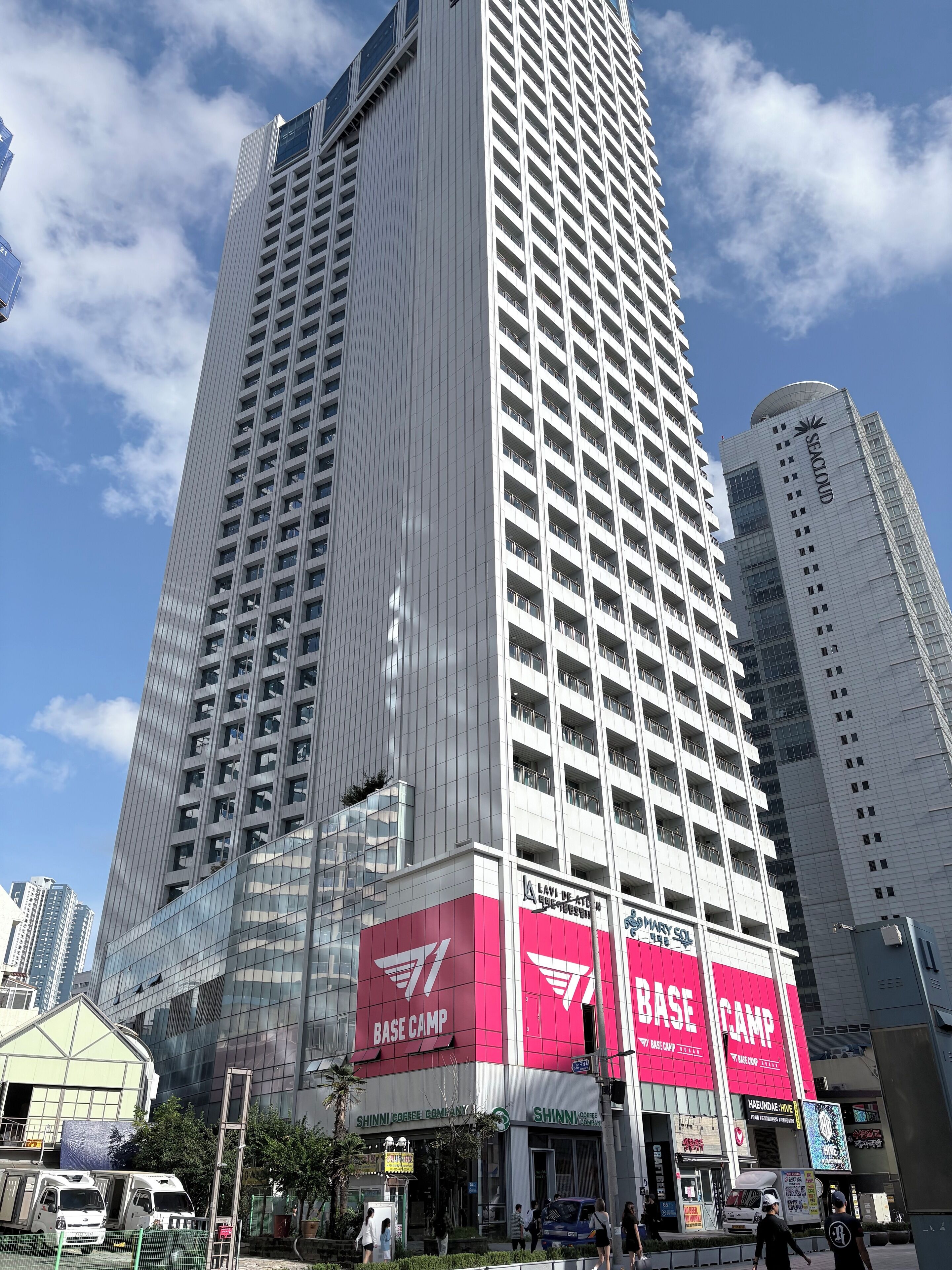 A tall building with multiple floors, featuring a prominent red and white sign for 'BASE CAMP' and 'SHINNI COFFEE'.