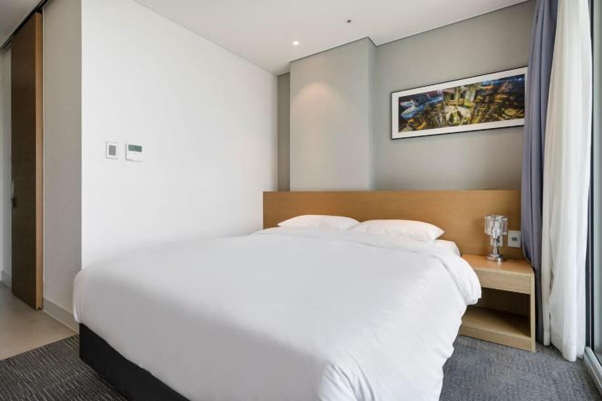 A hotel room with a large bed, a bedside table, a framed picture on the wall, and a window with curtains.