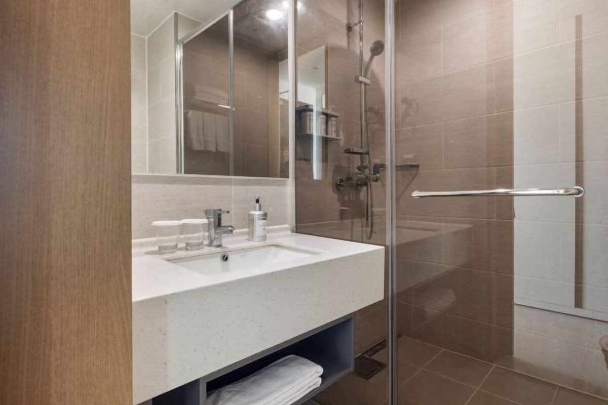 Een moderne badkamer met een glazen douchecabine, een witte wastafel en een spiegel.