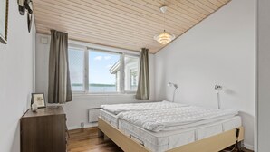 A bedroom with a wooden ceiling, a bed with a white mattress, a bedside table, a lamp, and a window with curtains. - Gorgeous home in ølsted with kitchen (Ølsted)