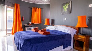 Une chambre à coucher comprenant un lit, deux lampes, une table de chevet, une fenêtre avec des rideaux et une œuvre d’art accrochée au mur.