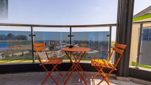Un balcon doté d’un plancher en verre, de deux chaises orange et d’une petite table ronde.