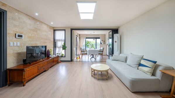 A spacious living room with a flat-screen TV, wooden cabinet, grey sofa, and a dining area with a table and chairs. - Gyeongju Hwangnaminn Pension (Gyeongju)