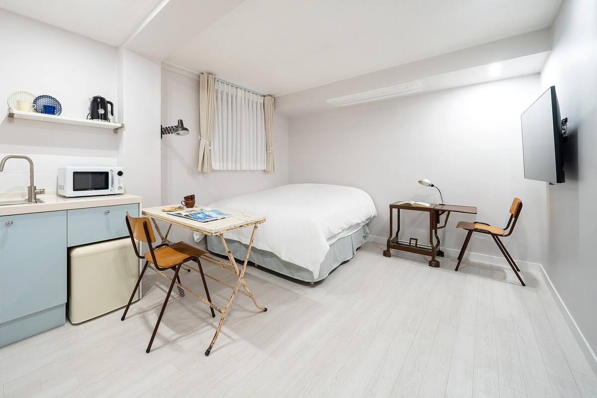 Ein kompaktes Hotelzimmer mit Küchenzeile, einem Bett, einem Schreibtisch und einem Fernseher.