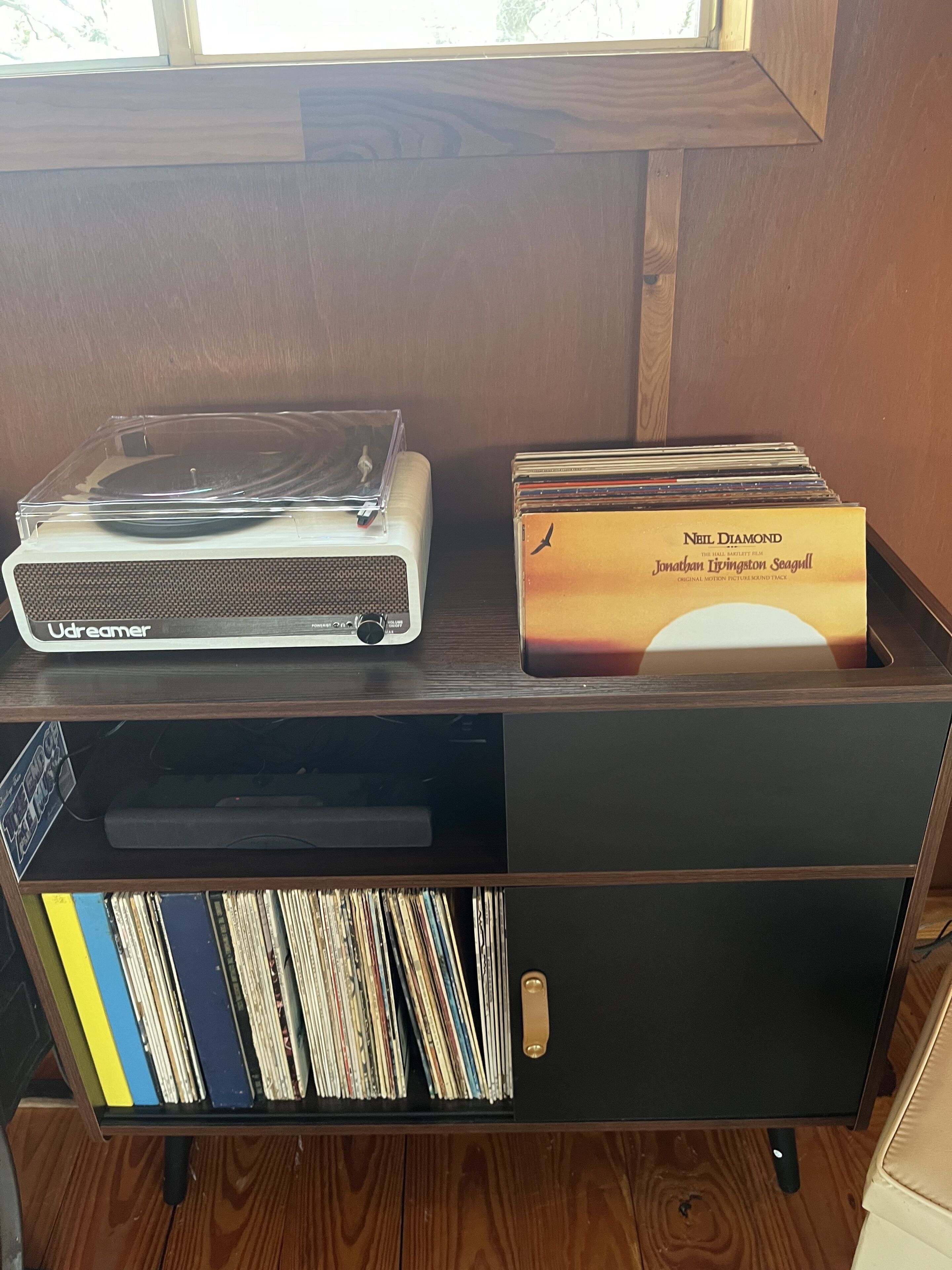 A wooden shelf with a turntable, a box of Neil Diamond's 'Sea Gull' album, and a CD rack filled with various albums.