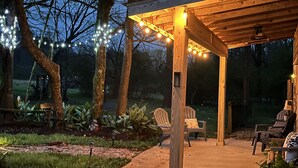Uma pérgola de madeira com luzes de cordão, área de estar ao ar livre e um caminho de jardim.