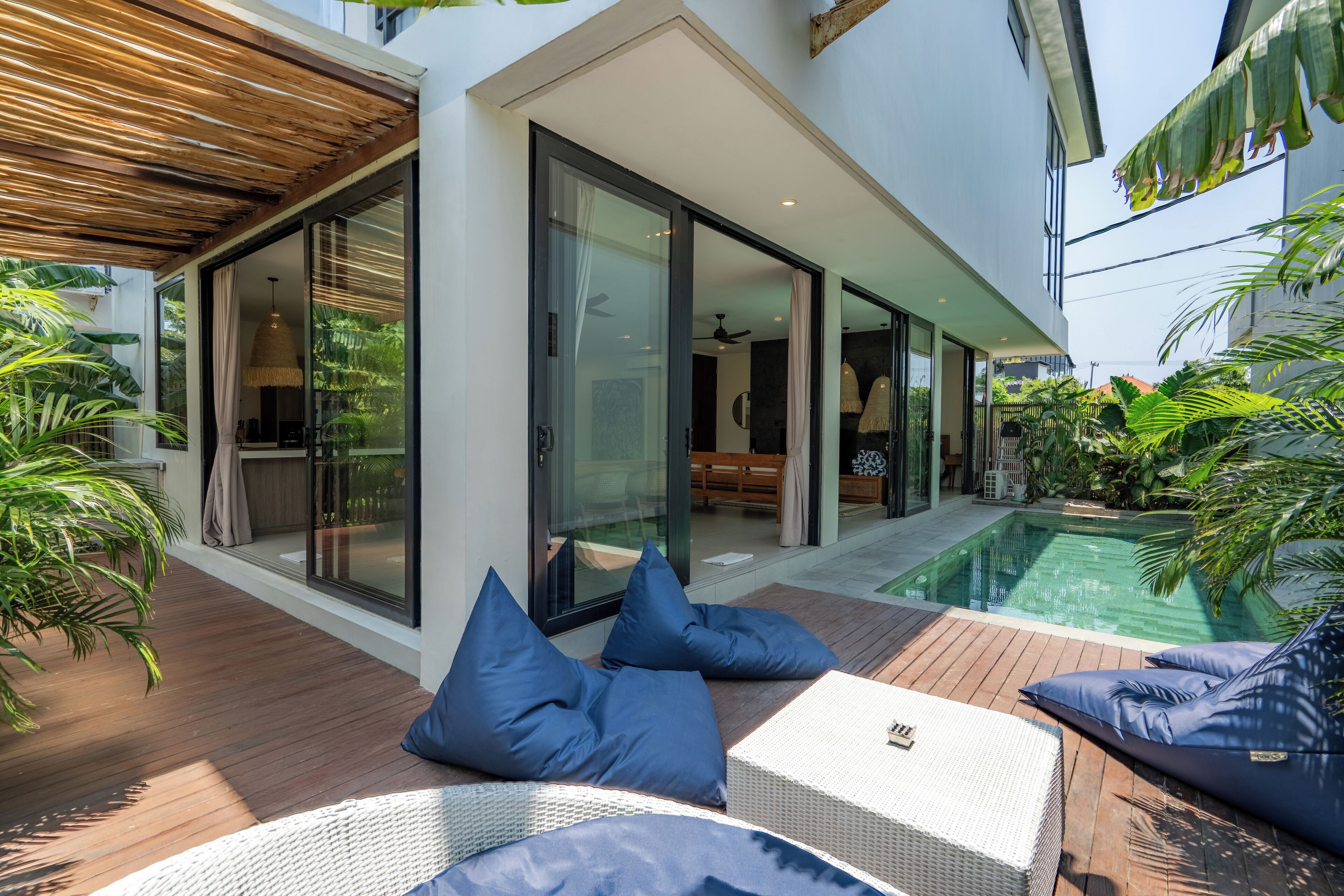 Een moderne woning met een glazen deur naar een zwembad, omringd door weelderige begroeiing.
