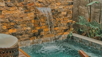 Relax by the soothing waterfall and pool, surrounded by lush greenery and a comfortable seating area.