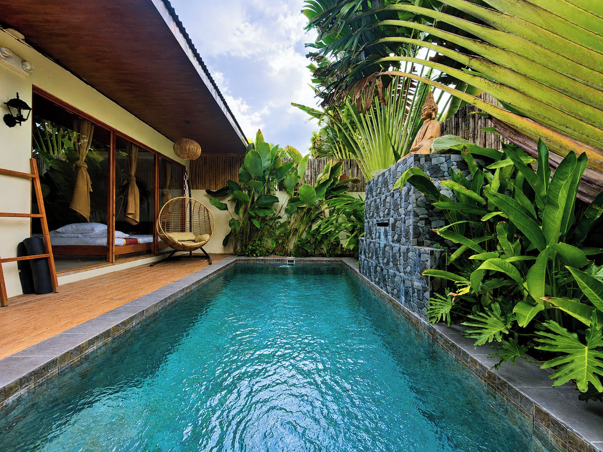 Una piscina con muro de piedra y plantas tropicales.