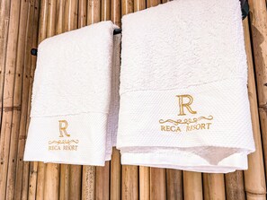 Two white towels with embroidered text and a letter 'R' on a bamboo background.