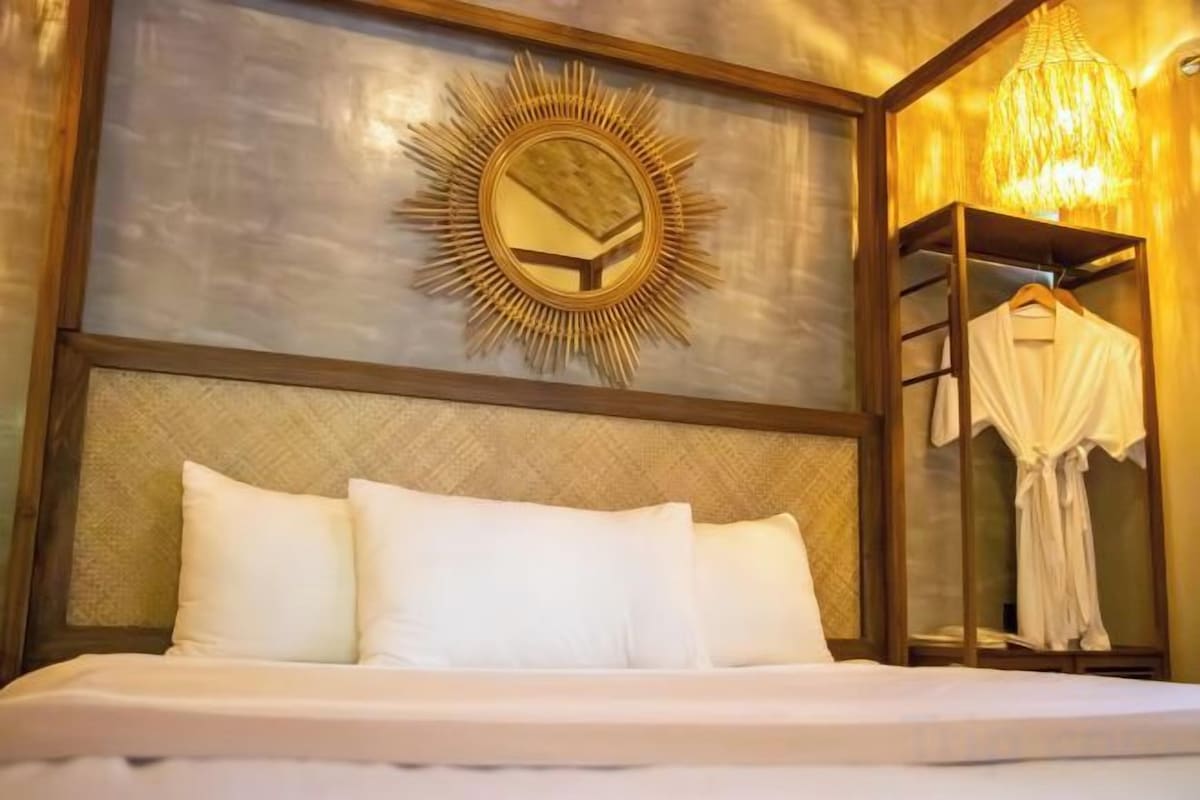 Habitación de hotel con cama, espejo con diseño de sol naciente y perchero.