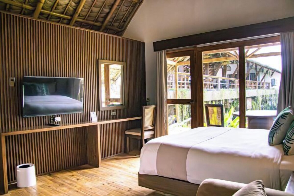 Un dormitorio con cama, televisor, ventana y vista a una estructura de madera en el exterior.