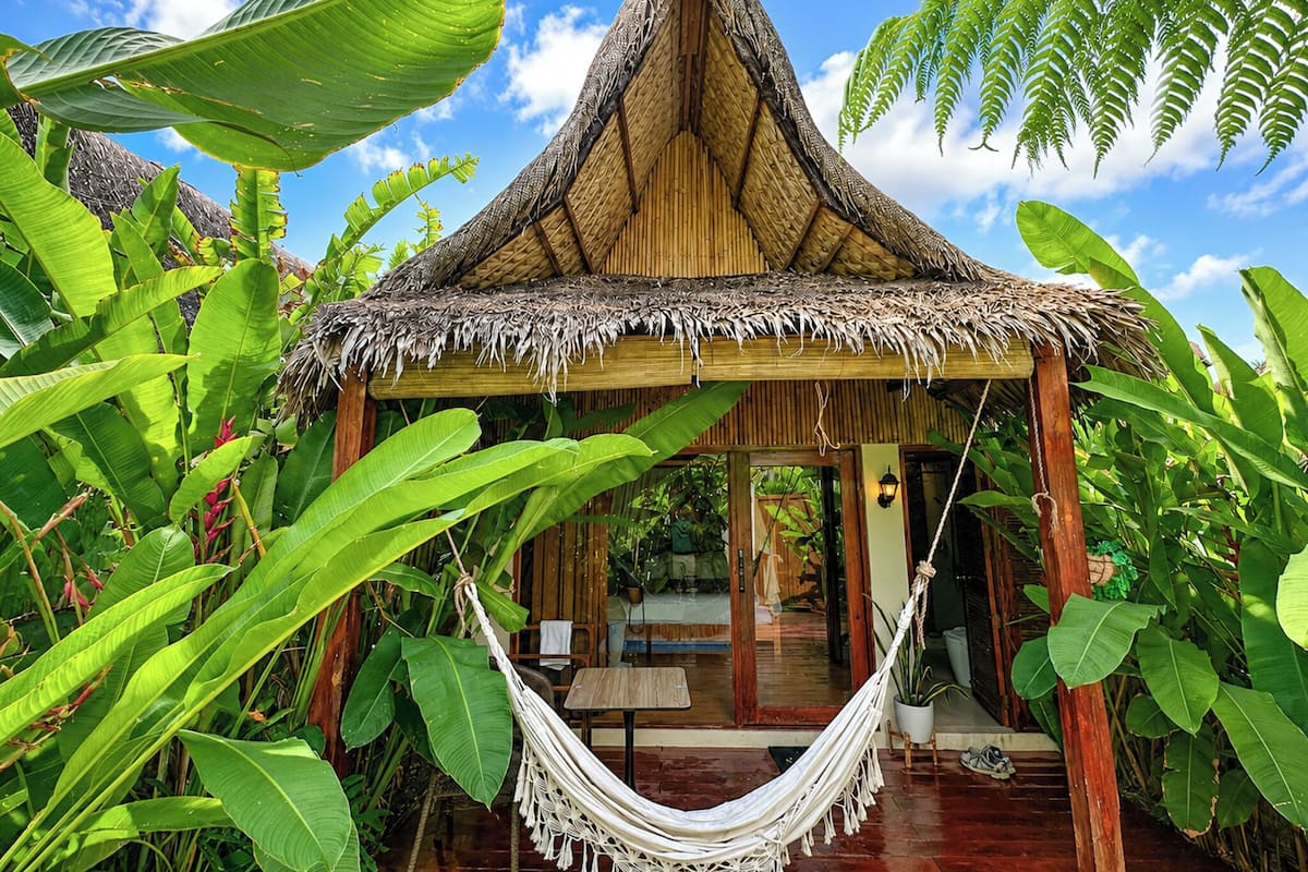 A thatched-roof hut with a hammock, surrounded by lush tropical foliage.